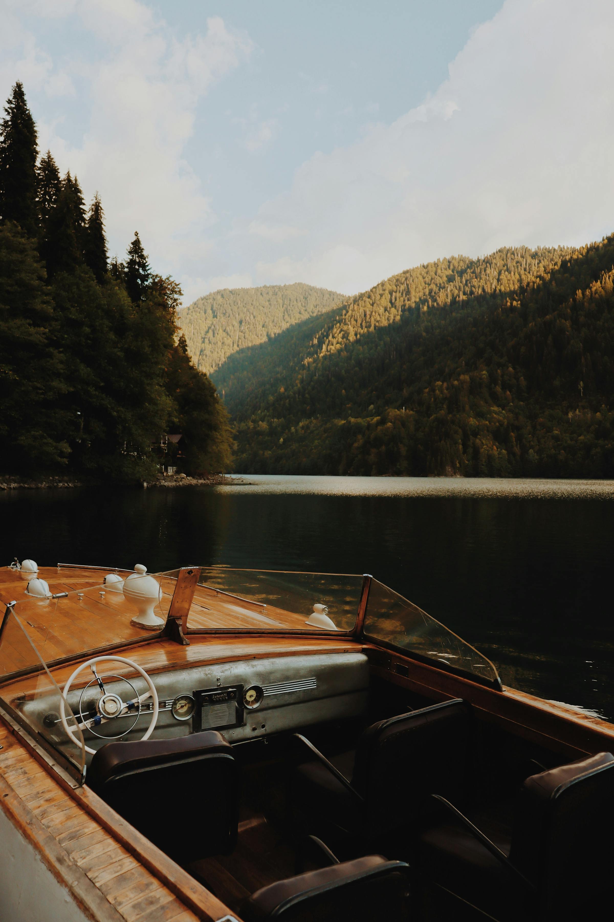 The helm of a wooden boat overlooking a calm mountain lake.
