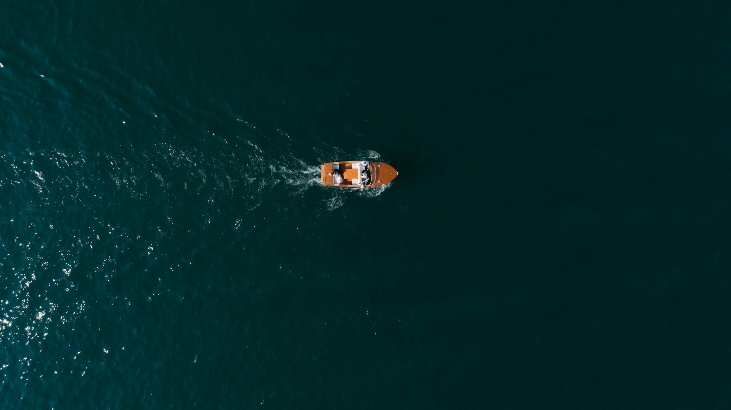 A wooden runabout cruising across vast open water from above.