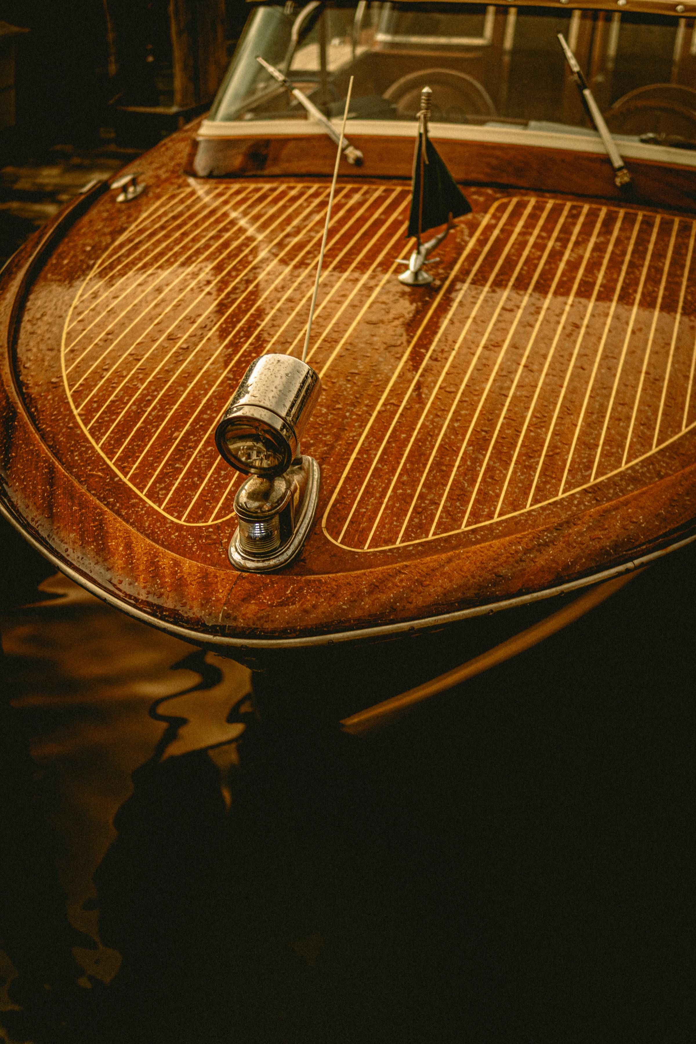 Detail of a polished mahogany bow with brass bow light and ensign on dark water.