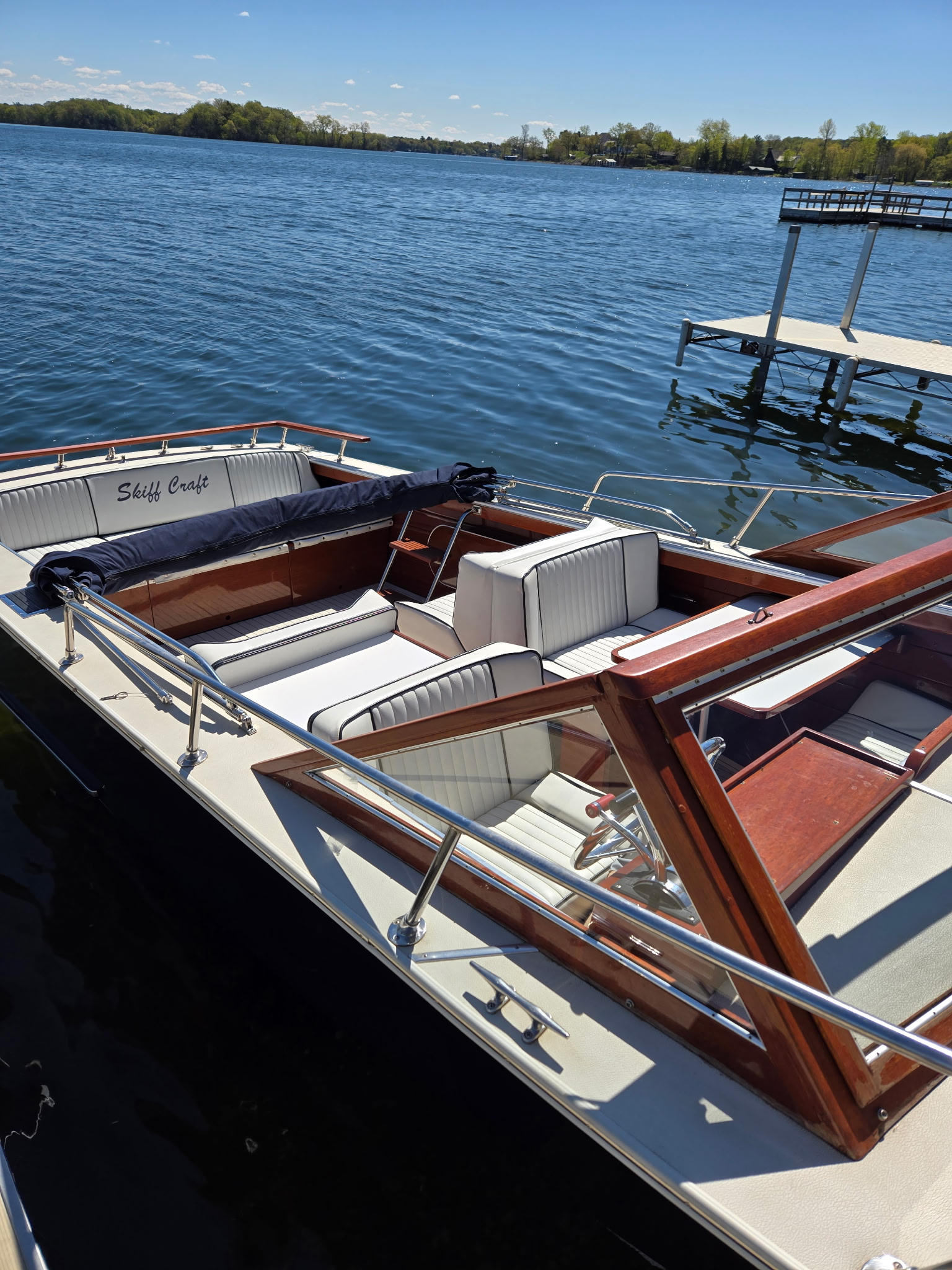 Skiff Craft cockpit from above at dock — white upholstery, mahogany trim, calm water behind.