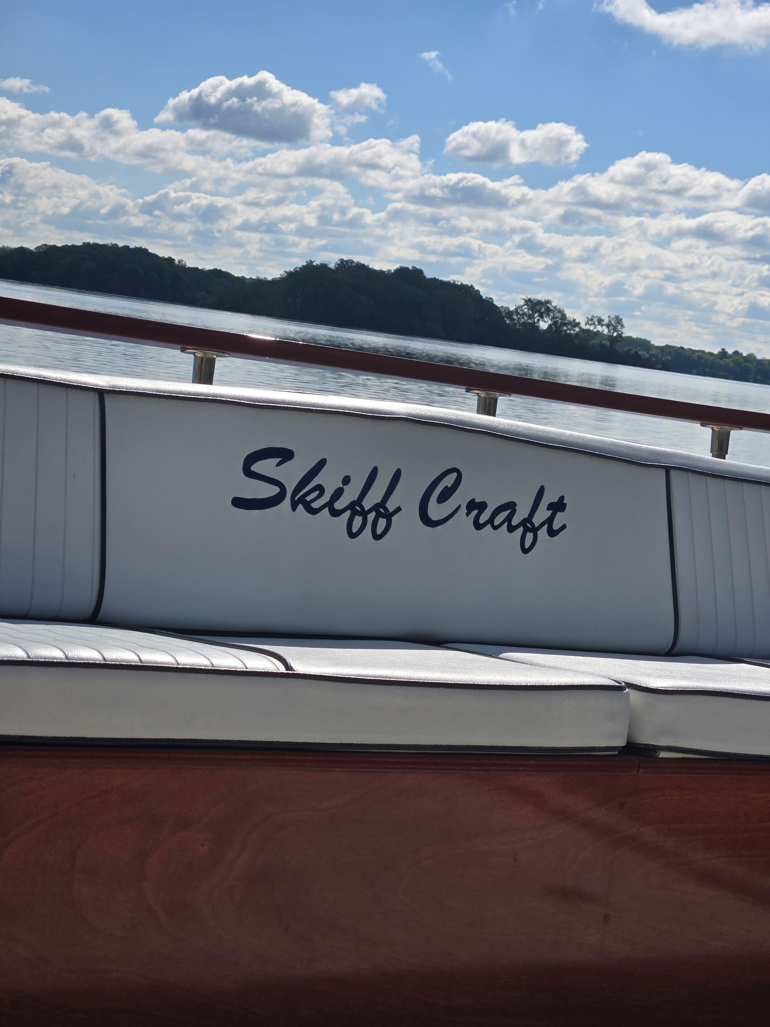 'Skiff Craft' embroidered in script on white upholstered seatback, lake and summer sky behind.